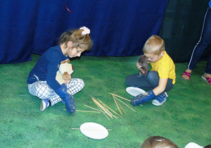 Dzieci na podłodze zbierają patyczki.