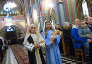 Dzieci w strojach jasełkowych stoją w kościele.Dziewczynka trzyma figurkę Jezusa.
