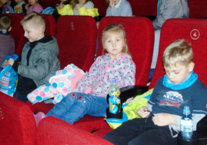 Dzieci siedzą na fotelach w sali kinowej.