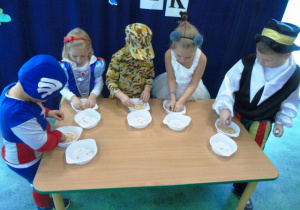 Grupa dzieci stoi przy stoliku i oddziela zairna w miseczkach