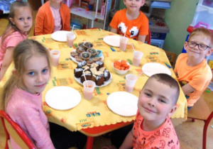 Dzieci siedza przy stoliku. Na stole stoi ciasto.