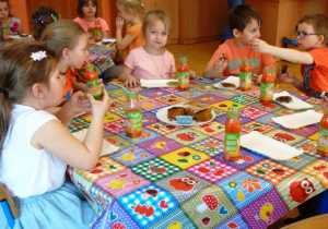 Dzieci siedzą przy stoliku i jedzą.