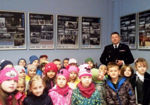 Dzieci stoją z komendantem. Na ściane dużo zdjęć.