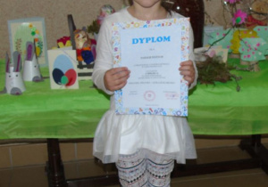 Dziewczynka stoi i trzyma dyplom.