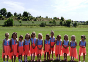 Dziewczynki w kolorowych sukienkach stoją na trawie.