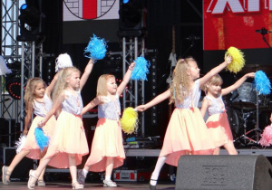 Dziewczynki tańczą na scenie. W rękach maja pompony.