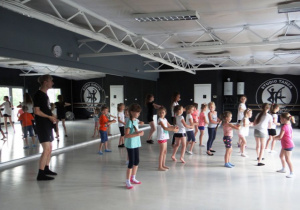 Dzieci tańczą z instruktorem na sali z lustrami.