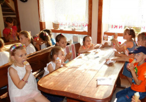Dzieci siedzą przy stole i jedzą lody.