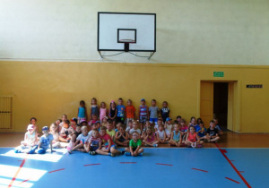 Dzieci siedzą na sali gimnastycznej.