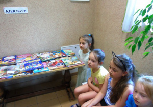 Cztery dziewczynki siedza naławce.Obok stolik na którym leżą książki.