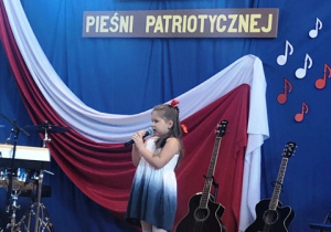 Dziewczynka stoi i śpiewa piosenkę.W tle napis " Konkurspiosenki patriotycznej".