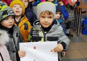 Dzieci stoją ustawione w budynku poczty. Jeden chłopiec trzyma list.