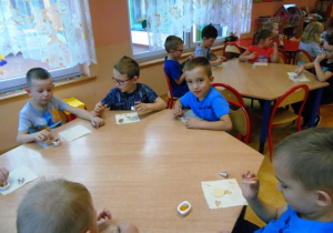 Dzieci siedzą przy stolikach i jedzą wafelki z miodem.