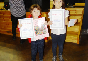 Dwie dziewczynki stoją i trzymają dyplomy.