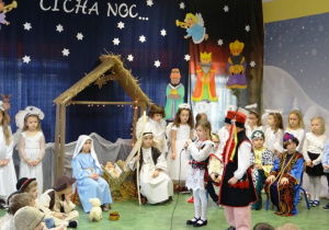 Dziewczynka w stroju krakowskim mówi wiersz, obok niej jestchłopiec w stroju krakowskim. Obok siedzi dzieczynka w niebieskiej sukience i chłopiec wstroju Józefa. Pomiędzy nimi stoi żłóbek z figurką Jezuska.