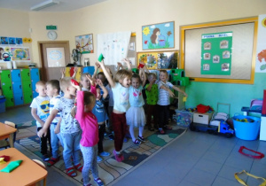 Dzieci bawią się na dywanie, mają podniesione ręce do góry.