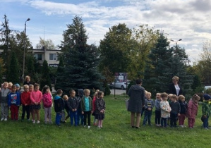 Dzieci stoja ustawione na ogródku przedszkolnym.