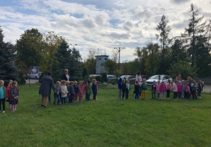 Dzieci stoją ustawione na ogródku przedszkolnym.