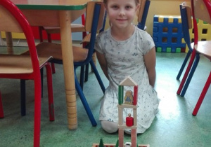 Dziewczynka siedzi na dywanie, przed nią budowla z klocków.