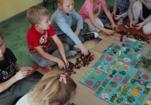 Dzieci siedzą na dywanie i robią wspólny plakat.