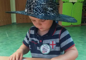 Chłopiec w kapeluszu siedzi przy stoliku i układa puzzle.