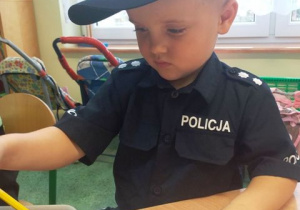 Chłopiec w stroju policjanta wybiera kredkę z koszyczka.