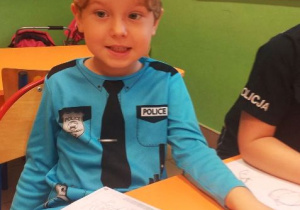 Chłopiec w stroju policjanta siedzi przy stoliku.