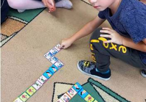 Dzieci na dywaie układaja domino.