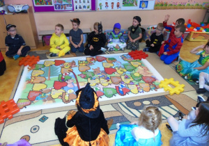 Dzieci siedzą na dywanie i grają w gre na dużej planszy.