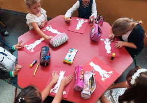 Dzieci siedza przy stolikach i wykonują pracę plastyczną.