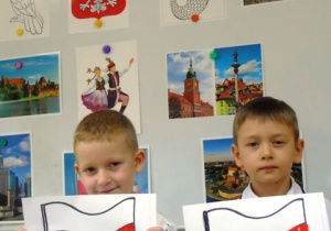 Chłopcy trzymają prace z flagami, w tle ilustracje przedstawiające Polskę.