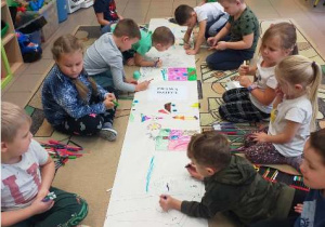 Dzieci siedzą na podłodze i kolorują na dużym arkuszu papieru.