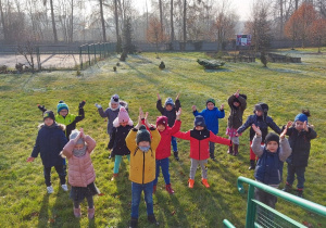Dzieci ubrane w kurtki i czapki ćwiczą w ogródku przedszkolnym.