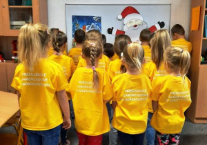 Dzieci stoją odwrocone plecami. Na żółtych koszulkach widać napis Przedszkole Samorządowe w Gorzkowicach.