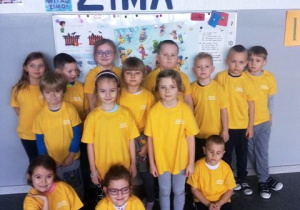 Dzieci w żółtych koszulkach stoją na sali.