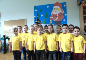 Grupa dzieci ubrana w żółte koszulki stoi na sali.