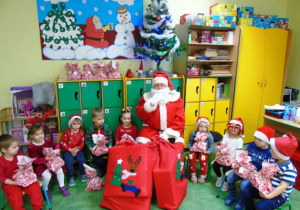 Dzieci siedzą na krzesełkach, obok nich Mikołaj.