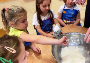 Dzieci wsypują mąkę do naczynia.