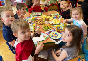 Dzieci w kolorowych strojach siedzą i jedzą poczęstunek.