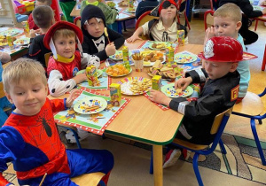 Dzieci w kolorowych strojach siedzą i jedzą poczęstunek.