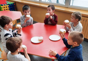 Dzieci siedzą przy stoliku i jedzą pączki.