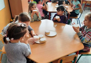 Dzieci siedzą przy stoliku i jedzą pączki.