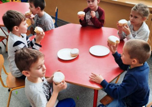 Dzieci siedzą przy stoliku i jedzą pączki.