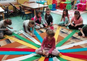 Dzieci siedzą na dywanie, bawią się wiatrakiem matematycznym.