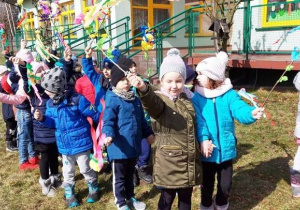 Dzieci stoją w ogrodzie przedszkolnym i trzymają gaiki.