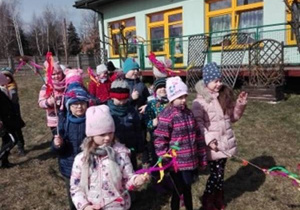 Dzieci stoją w ogrodzie przedszkolnym i trzymają gaiki.