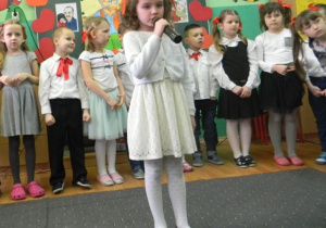Dziewczynka ubrana na biało mówi do mikrofonu
