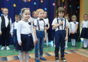 Troje dzieci stoi na środku sceny jeden chłopiec trzyma w ręku mikrofon