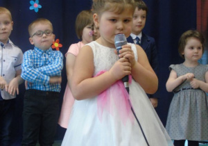 Dziewczynka w białej sukni z kwiatami trzyma mikrofon