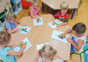 Dzieci siedzą przy stoliku tworząc pracę plastyczną na temat dowolny.